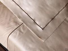 Detail of the sheets and pillowcases in wood-coloured satin with contrasting cordonnet