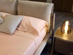 Detail of the upholstered headboard of the Cayman bed, with upholstered cushion, matching bed frame and high wooden and metal feet