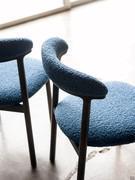 Detail of the curved backrest with lower profile in solid wood and upholstered support covered in fabric