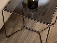 Focus on the slender tubular metal structure which forms a cross on the floor, and frames the fumé glass top in the upper section