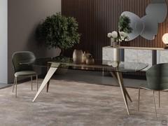 Table Pegaso with 200 cm barrel top made of clear glass: the base with pointed legs is made of champagne-painted metal to match the frame of chairs and sideboard to create a coordinated living room