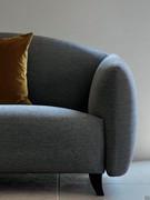 Detail of the rounded, rounded volumes of the Gilmour sofa, supported by high, arched dark wood feet