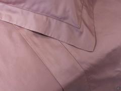 Détail des draps et des taies d'oreiller en satin mauve avec ourlets